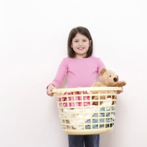 young girl holding laundry basket of clothes and toys