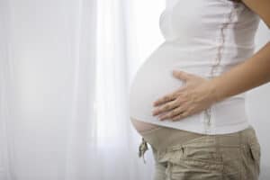 picture of a pregnant mother standing in front of a window with her hand on her pregnant belly