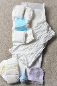 picture of hospital freebies including large postpartum pads, regular menstrual pads, baby diapers, baby hat, bulb syringe