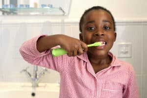 picture of a preschool-aged girl brushing her teeth as part of her household responsibilities