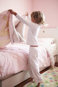 picture of a preschool-aged girl making her bed as one of her household chores