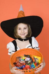 picture of a young girl dressed in a witch costume holding a bucket of Halloween candy