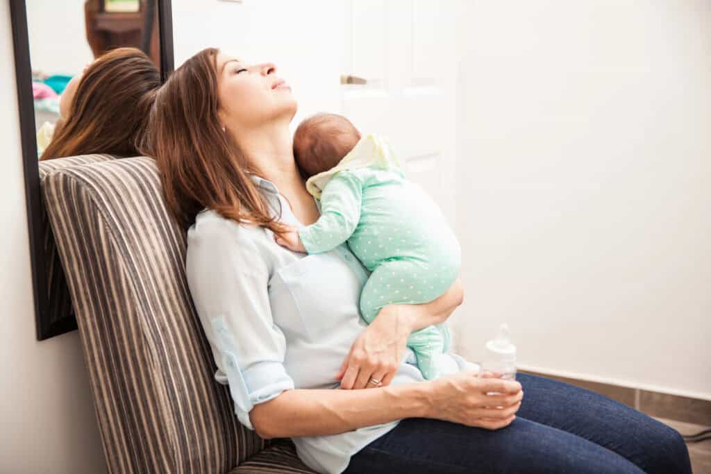 picture of a tired mom sitting in a chair holding her baby