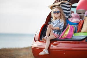 picture of a little girl ready for a family road trip sitting in the back of a car 