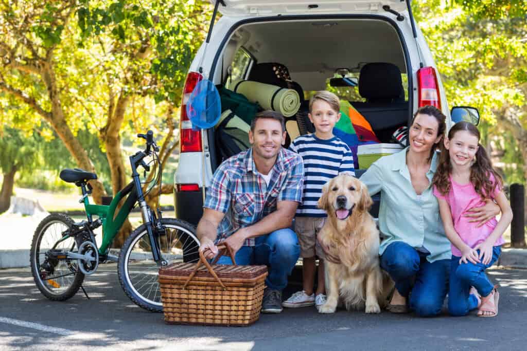 picture of a family standing at the back of their car posing for a picture with their dog while getting ready for a family road trip