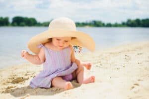 picture of a baby girl wearing a sunhat playing in the sand at the beach