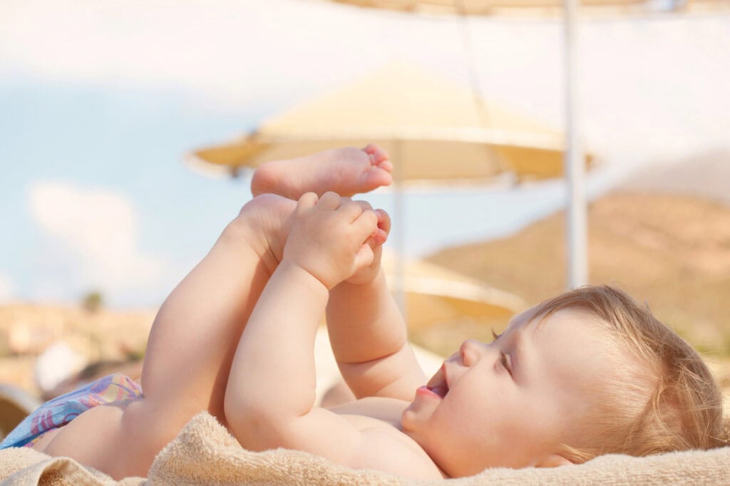 baby playing with their toes while lying in the sand at the beach