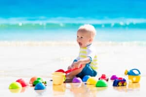 picture of a baby sitting on the beach at the ocean wearing a baby swimsuit playing with beach toys for a baby