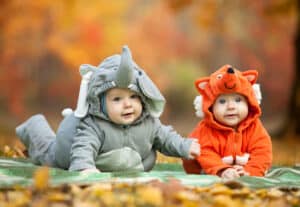 picture of two babies wearing infant halloween costumes; one is wearing an infant elephant costume and the other is wearing a infant fox costume for halloween