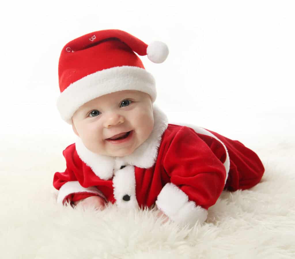 Happy Smiling baby lying on tummy wearing a red and white Christmas Santa hat and suit, isolated on a white background.