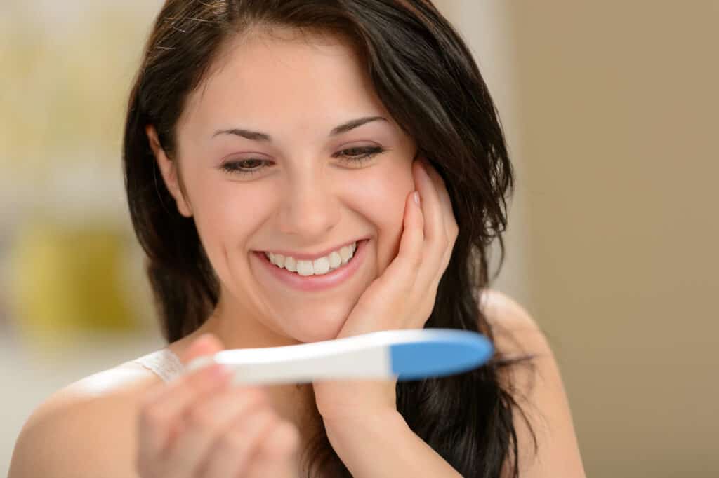 picture of a woman smiling while looking at a positive pregnancy test