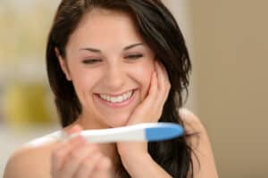 picture of a woman smiling while looking at a positive pregnancy test