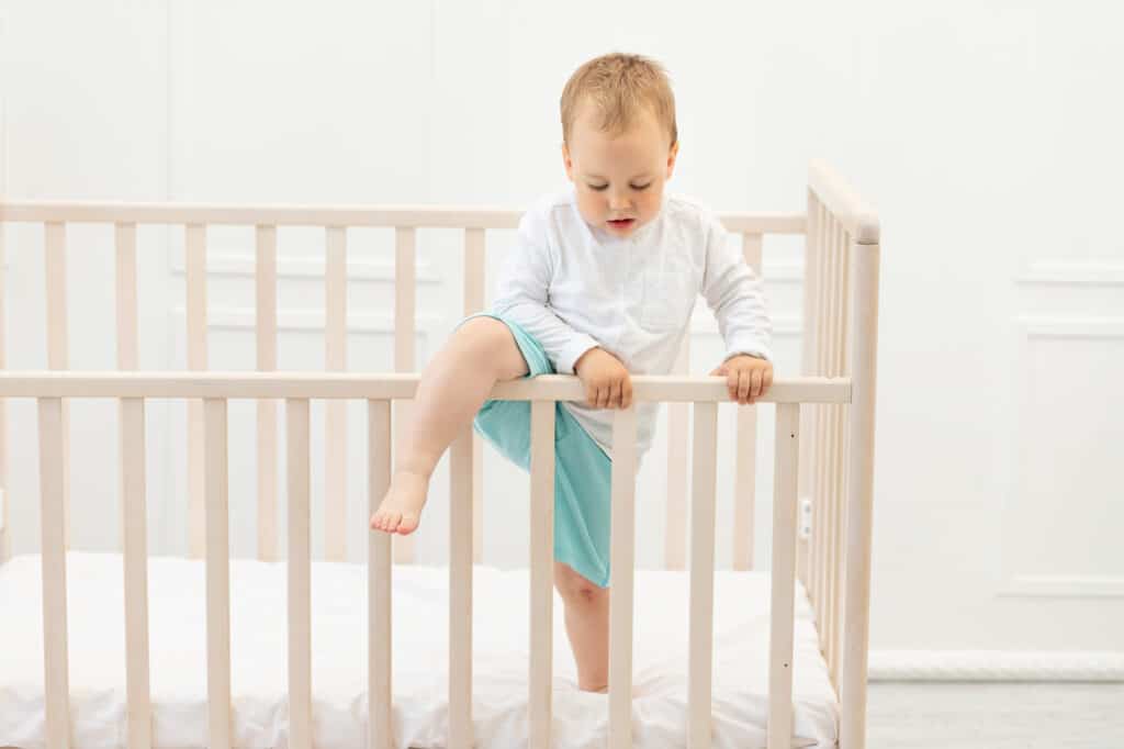  young child trying to climb out of the crib