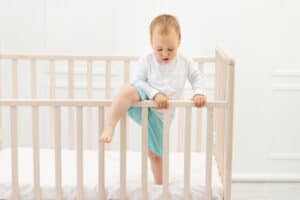  young child trying to climb out of the crib