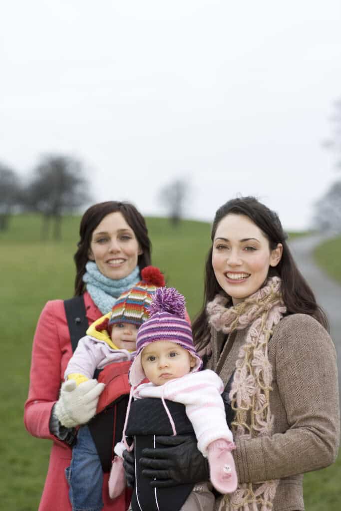 Two mothers with babies in baby carriers in park