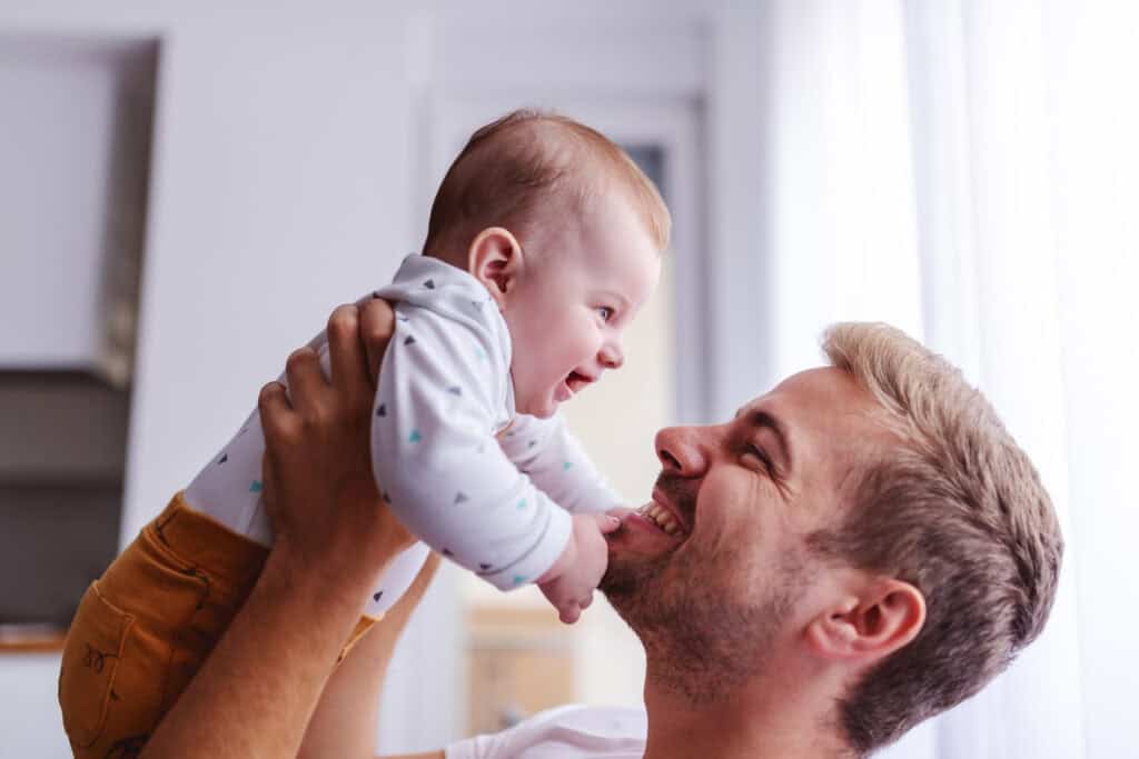 a new dad smiling while holding a smiling baby up in the air