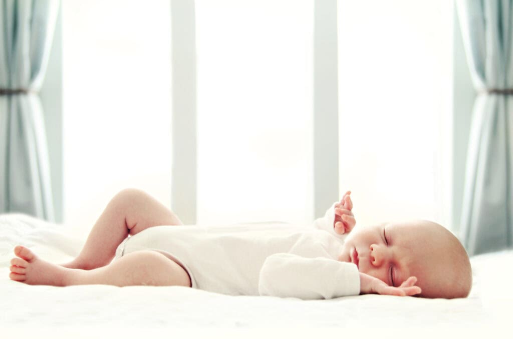 Newborn baby sleeping on white blanket in front of a window