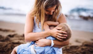 picture of a breastfeeding mom wearing a breastfeeding swmisuit while nursing at the beach