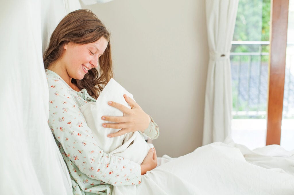 woman wearing a postpartum pajamas while holding her nerbown baby