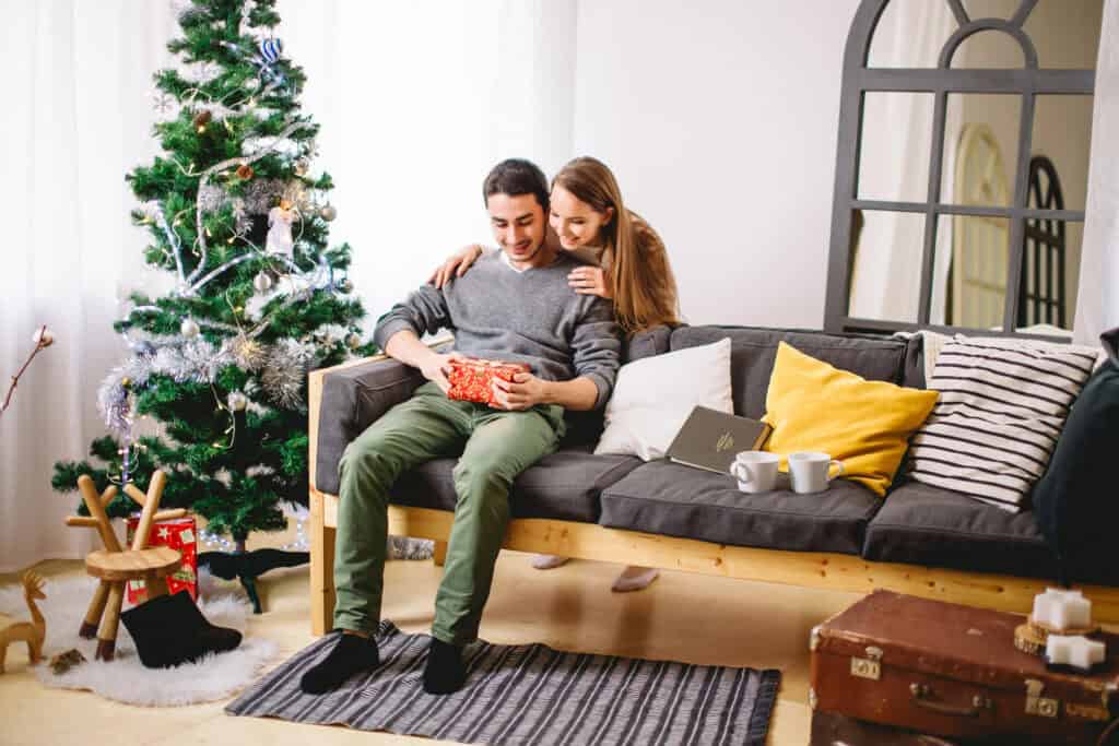 wife giving her husband a Christmas gift by a Christmas tree