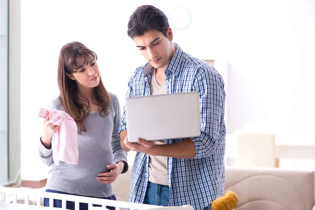 a pregnant woman and her husband looking at a computer learning how to financially prepare for a baby