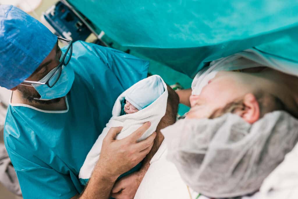 picture of a husband holding a baby next to the mother in the OR after an unplanned c-section