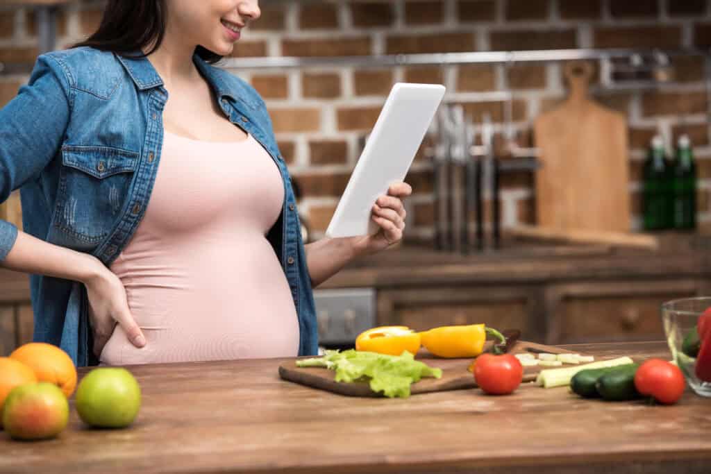 picture of a pregnant woman in the kitchen with healthy foods on the counter