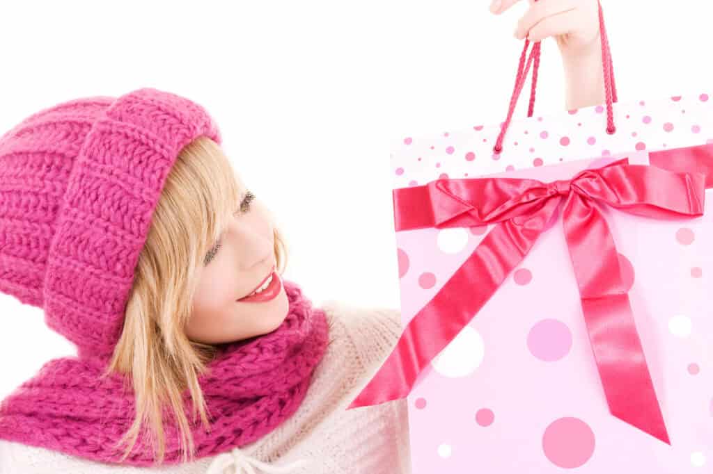 picture of a tween girl wearing a pink winter hat holding up a pink gift bag