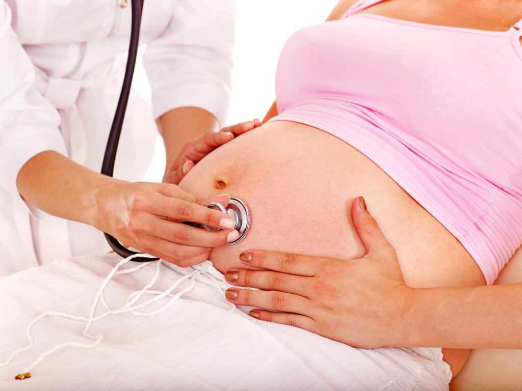 picture of a woman's pregnant belly being checked out with the stethoscope by a care provider