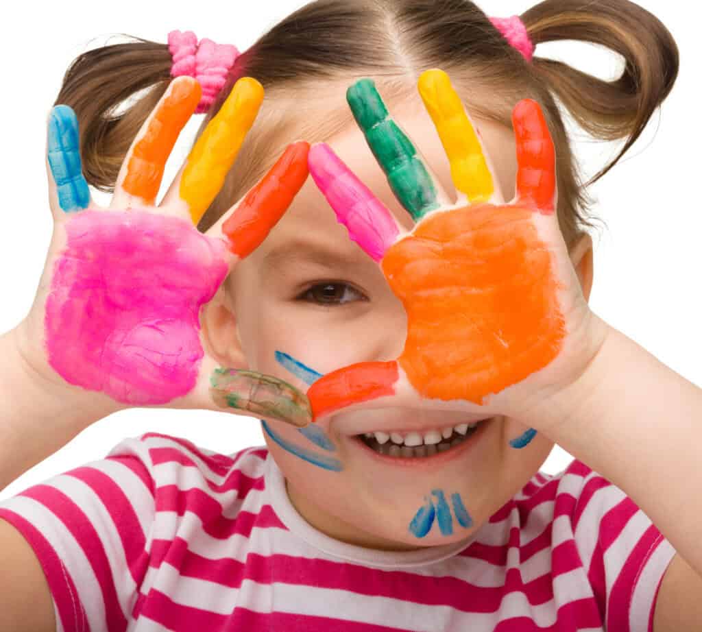 picture of a girl in Kindergarten holding her hands up to her face with her hands painted all different colors