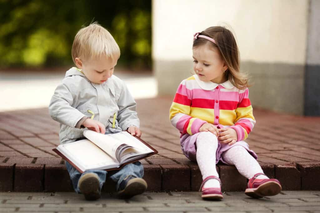 picture of a preschool-aged boy and girl sitting on the sidewalk looking at a Christian picture book for kids