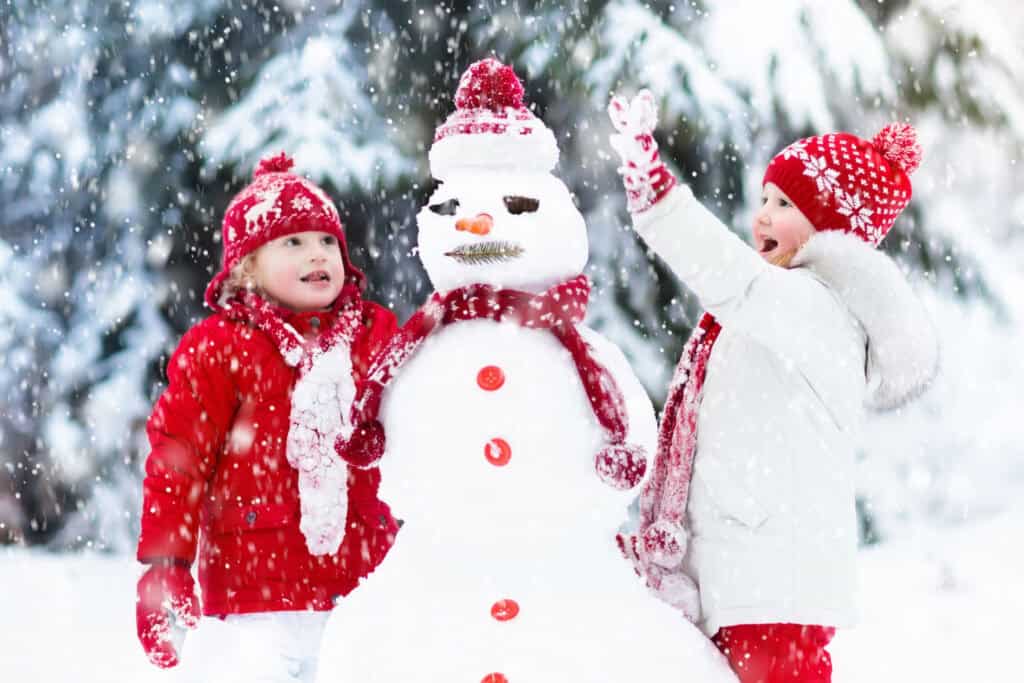 two young kids building a snowman outside in the snow at Christmastime