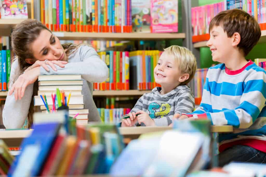 picture of a burned out homeschool mom laying her head on a stack of books at the library while her kids are doing their homeschool work smiling at her