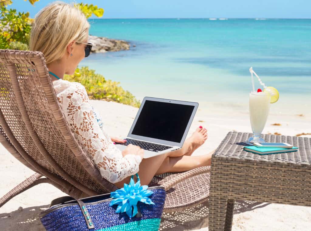 picture of a homeschool mom sitting at the beach working on homeschool planning on her computer with a drink on the table beside her