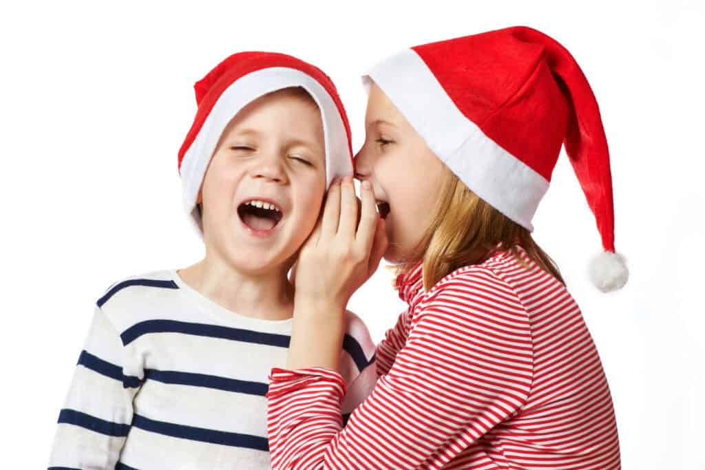 picture of two kids wearing Santa hats with a girl telling a boy a Christmas joke