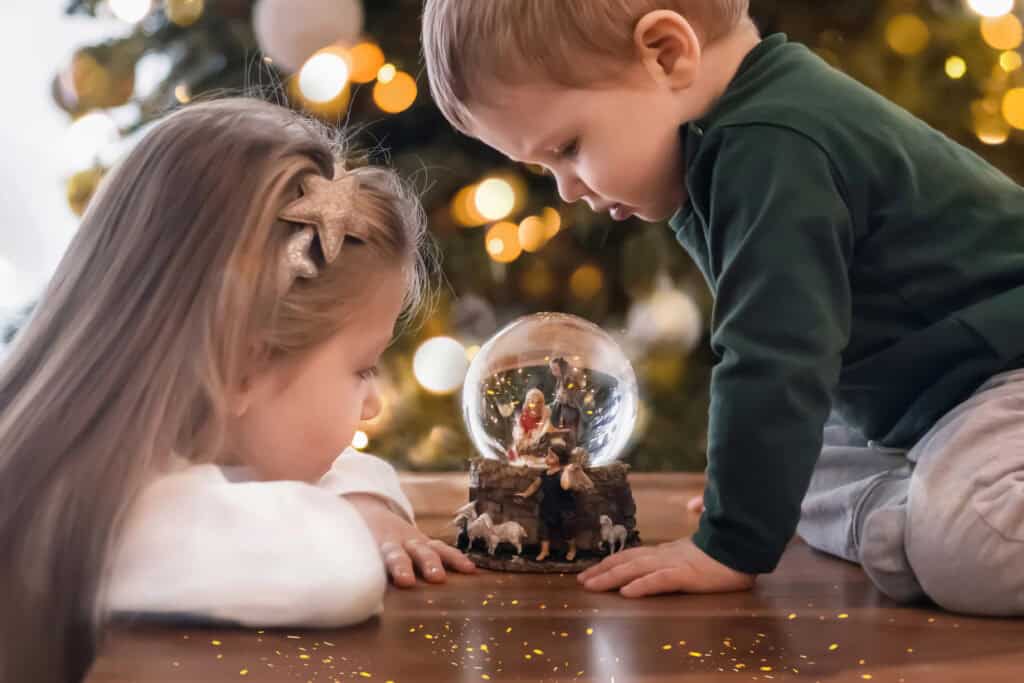 two young children looking at a Nativity scene snow globe while celebrating Advent