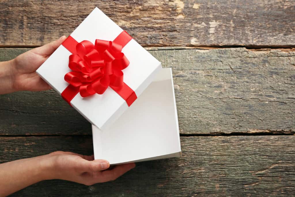 picture of a teenage boy opening a white gift box with a wooden background