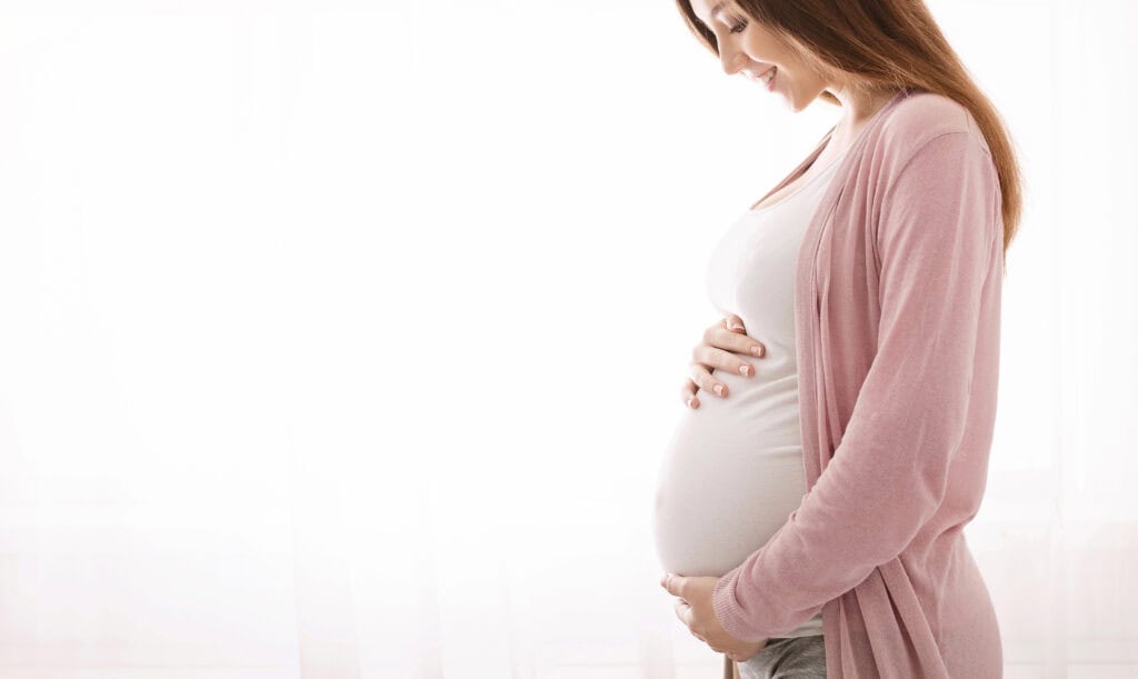 pregnant woman looking down at her pregnant belly and smiling while getting maternity pictures