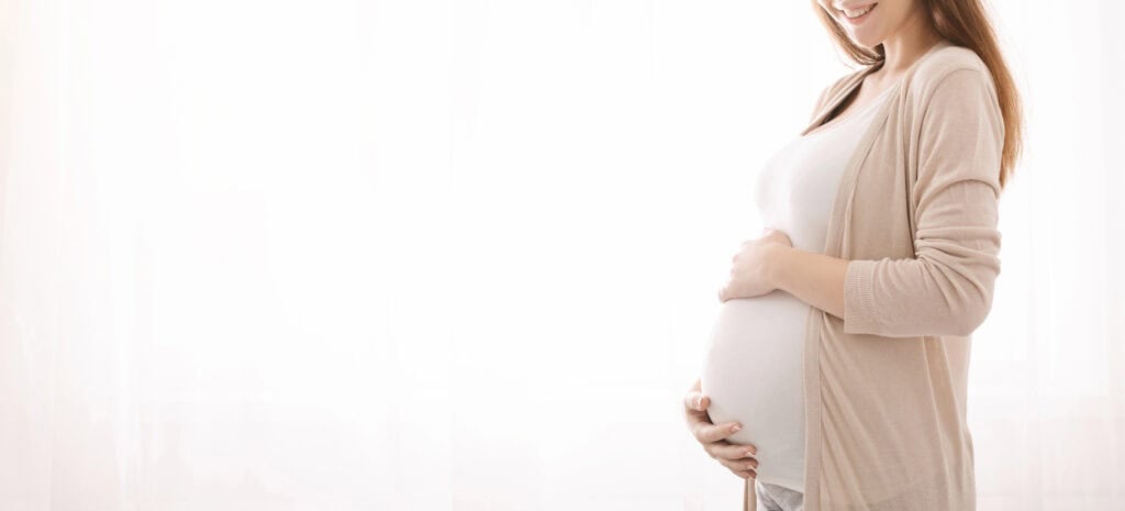 pregnant woman smiling at the camera with her hands around her pregnant belly